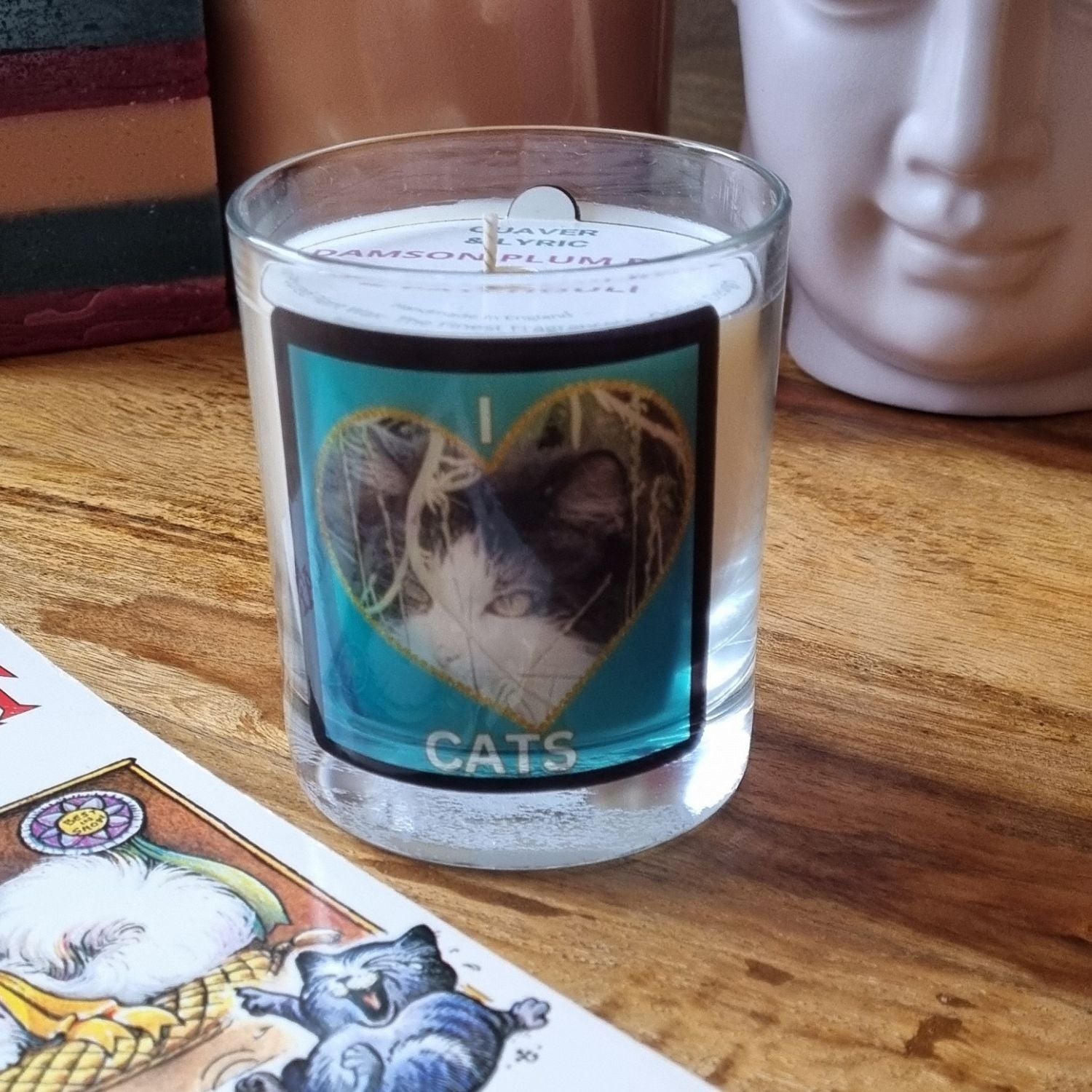 scented candle in glass container with fluffy black and white cat in a heart love cats design on a table