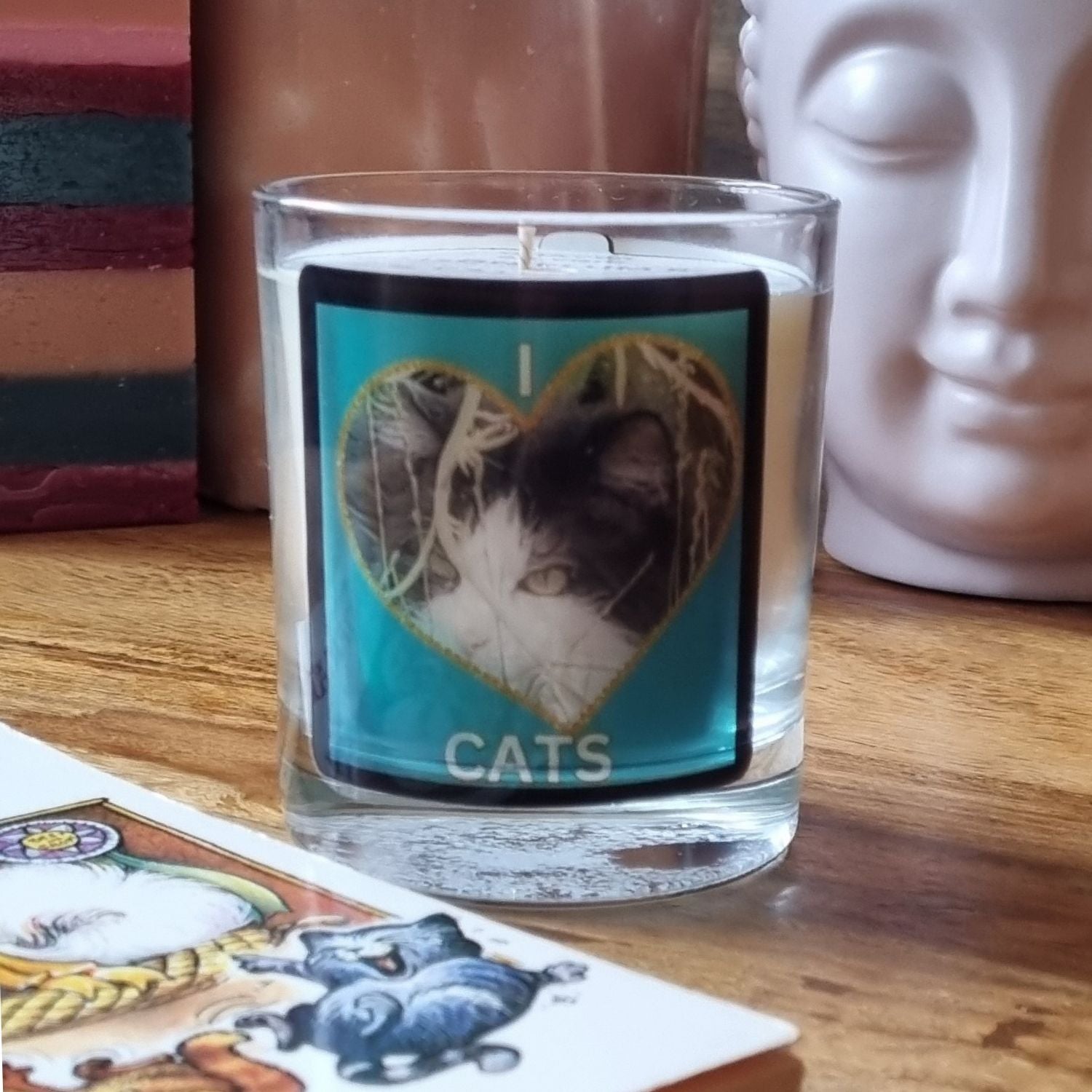 scented candle in glass container with fluffy black and white cat in a heart love cats design on a table