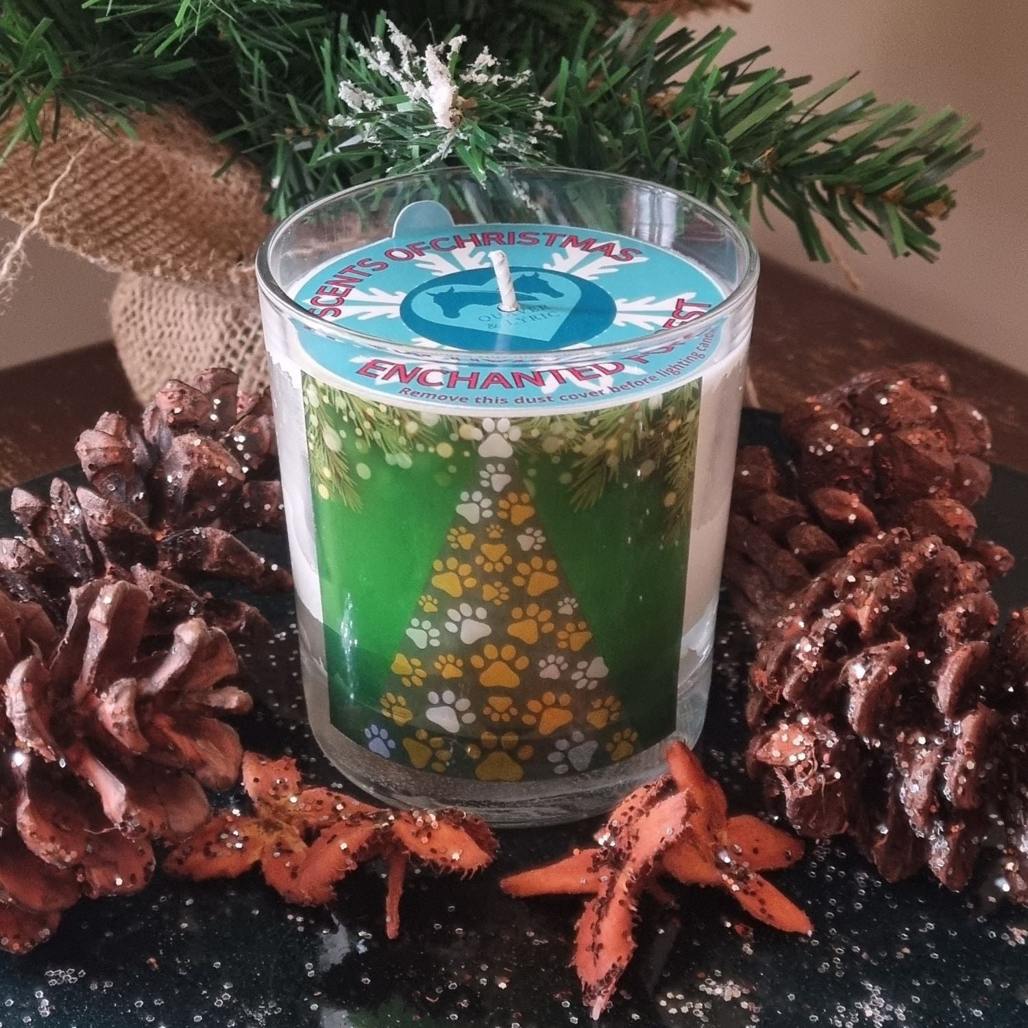 A Christmas scented candle with a Christmas Tree made from yellow and white paws design surrounded by sparkling pine cones.