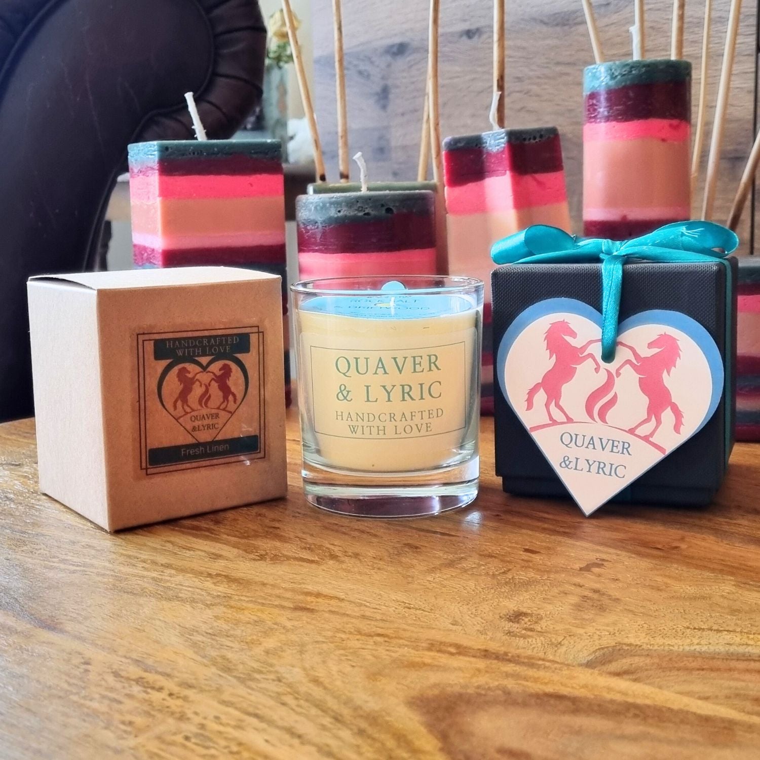 a scented candle with quaver and lyric handcrafted with love label next two a kraft box and black luxury gift box on a table with other candles