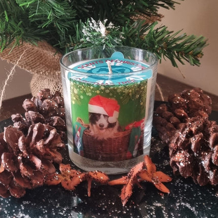 a christmas scented candle in a glass container with a festive collie dog in a santa hat design, surrounded by glittery pine cones