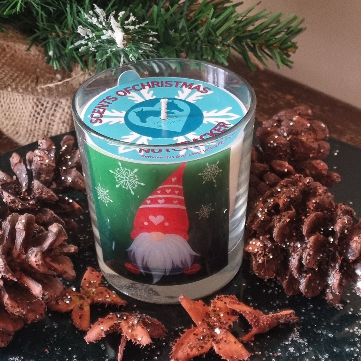 a scented candle in a glass container with a Christmas gonk design surrounded by glittery pine cones