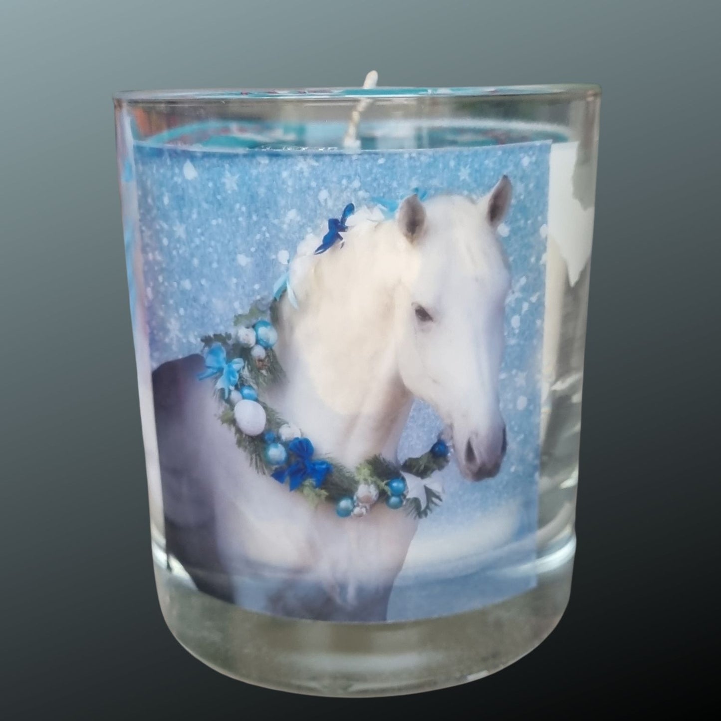 a scented candle in a glass container with a grey horse wearing a festive garland on his neck