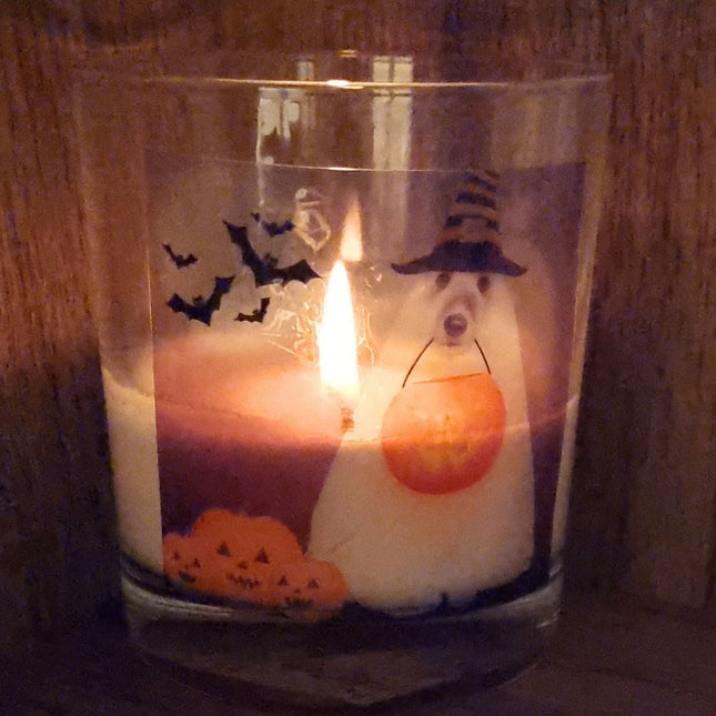 A burning scented Halloween candle featuring a spooky dog in a sheet dressed as a ghost with a trick or treat pumpkin bowl