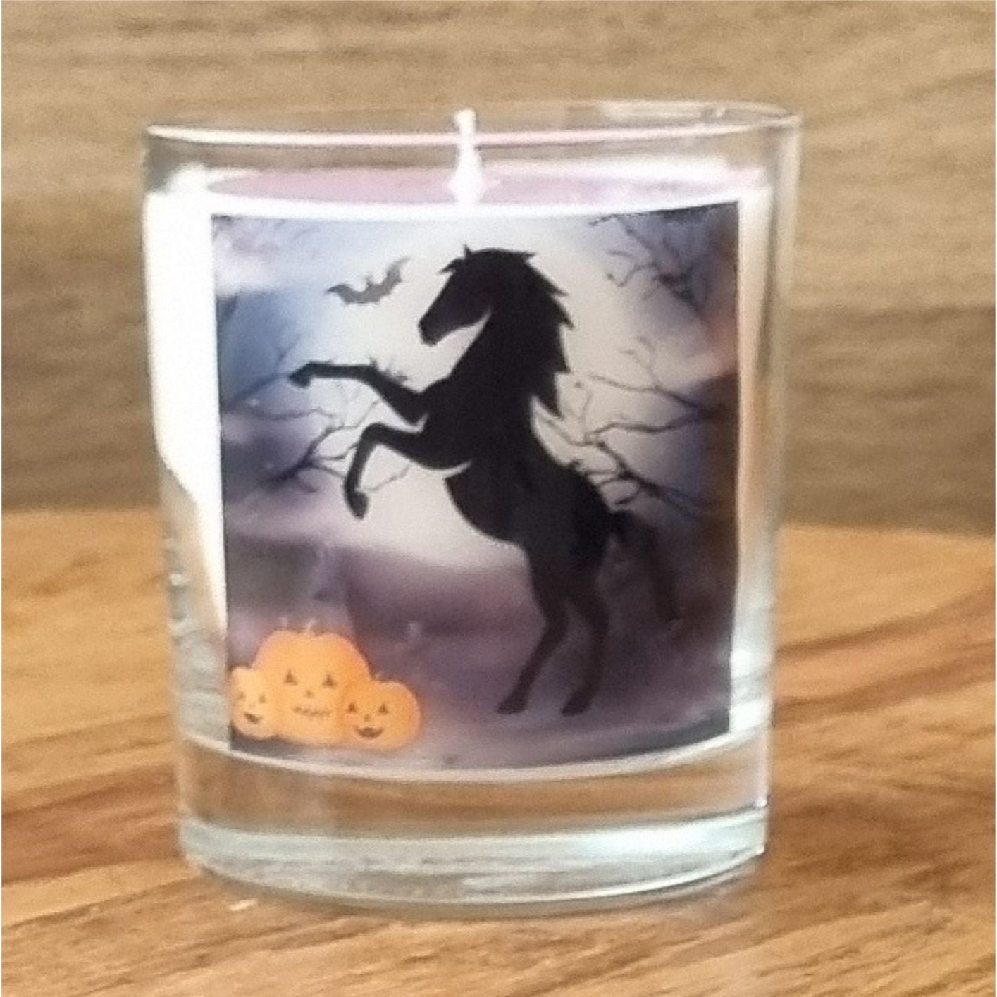 a scented halloween candle in a glass container with a black rearing horse and pumpkins in a graveyard setting