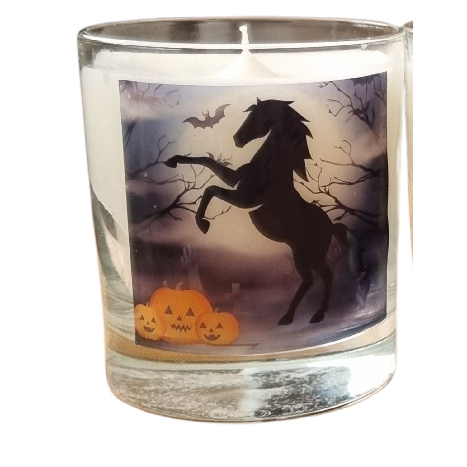 a scented halloween candle in a glass container with a black rearing horse and pumpkins in a graveyard setting