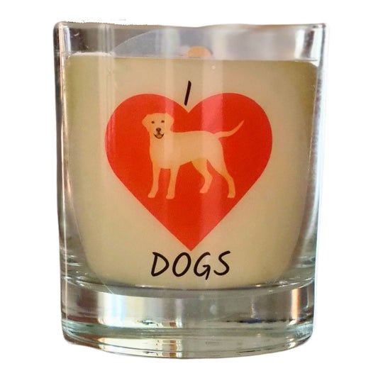 A colourless glass containing white candle wax. On the glass horizontally from the top is I then a large red heart and dogs written underneth. In the heart is a picture of a yellow labrdor dog.