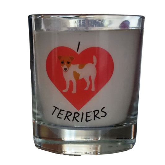 A colourless glass containing white candle wax. On the glass horizontally from the top is I then a large red heart and terriers written underneth. In the heart is a picture of a brown and white jack russell terrier dogr dog.