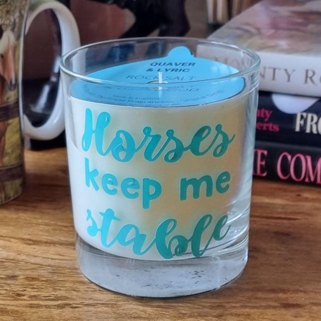 The Quaver&Lyric Scented Candle In Glass Container, featuring Horses Keep Me Stable text, rests on a wooden surface with books and a mugâ€”an ideal gift for horse lovers, offering premium fragrances.