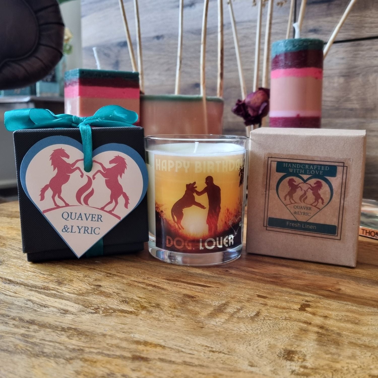 Three candles on wood: a handmade candle in a gift box with a heart-shaped tag of two horses, a Quaver&Lyric Scented Candle In Glass Container Happy Birthday Dog Lover Gift, and a box labeled Handcrafted with Love, Fresh Linen premium fragrances.