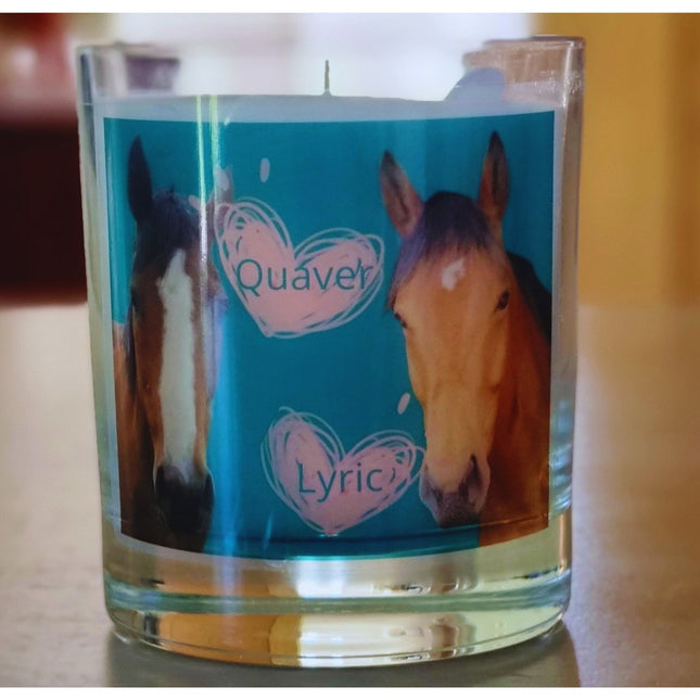 The Quaver&Lyric Scented Candle In Glass Container features a label with two horses on blue, white hearts framing Quaver and Lyric. Enjoy premium fragrances for a delightful scented experience.