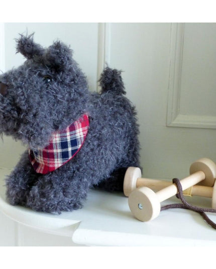 a soft toy scottie dog  with grey fur and a plaid neckerchief next to the detachable wheels that turn him into a pull along toy.