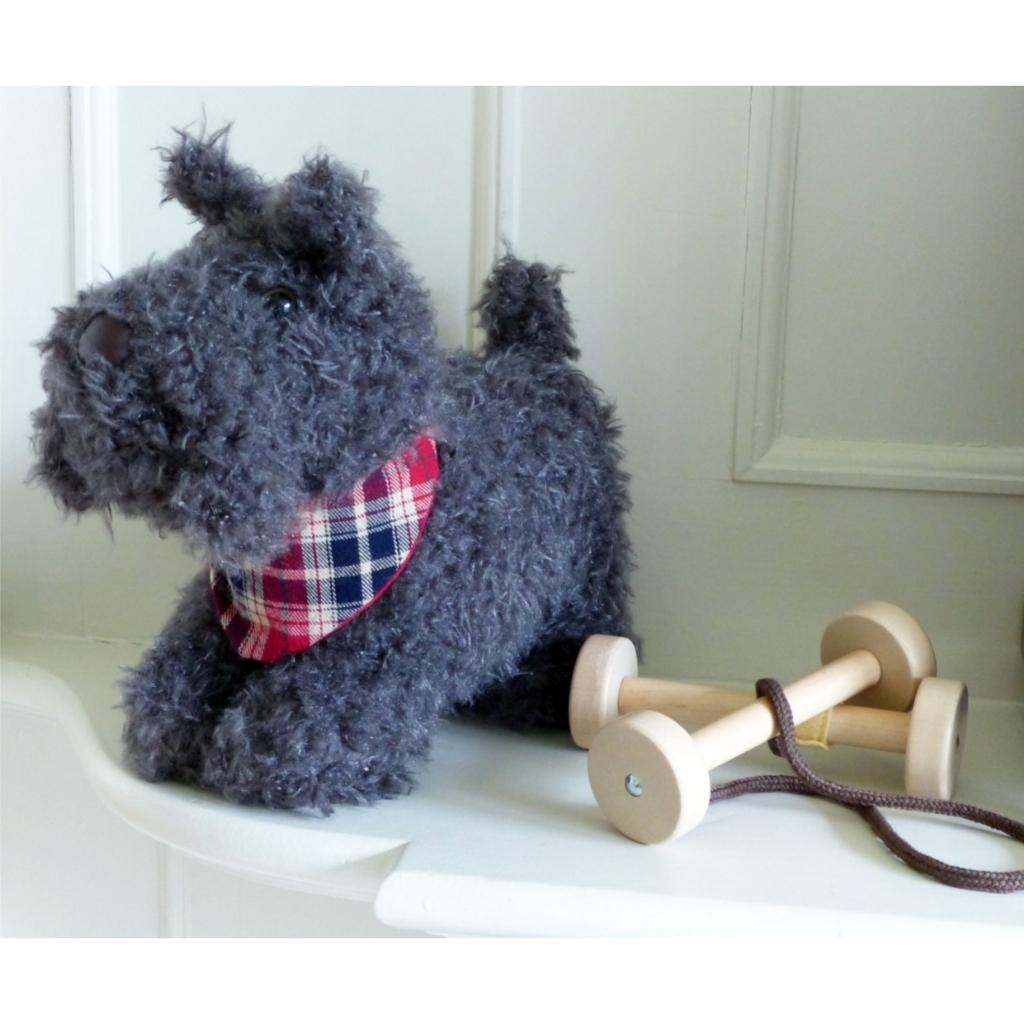 a soft toy scottie dog  with grey fur and a plaid neckerchief next to the detachable wheels that turn him into a pull along toy.