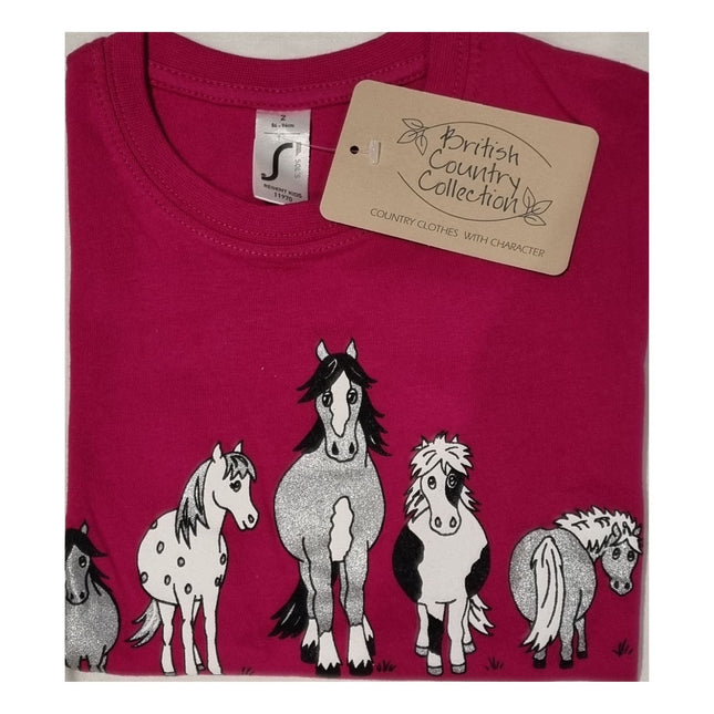 The Childrens T Shirt Printed The Herd Horse Design by British Country Collection is a folded pink 100% cotton tee featuring five uniquely patterned cartoon horses and a beige brand tag. Machine washable for easy care.