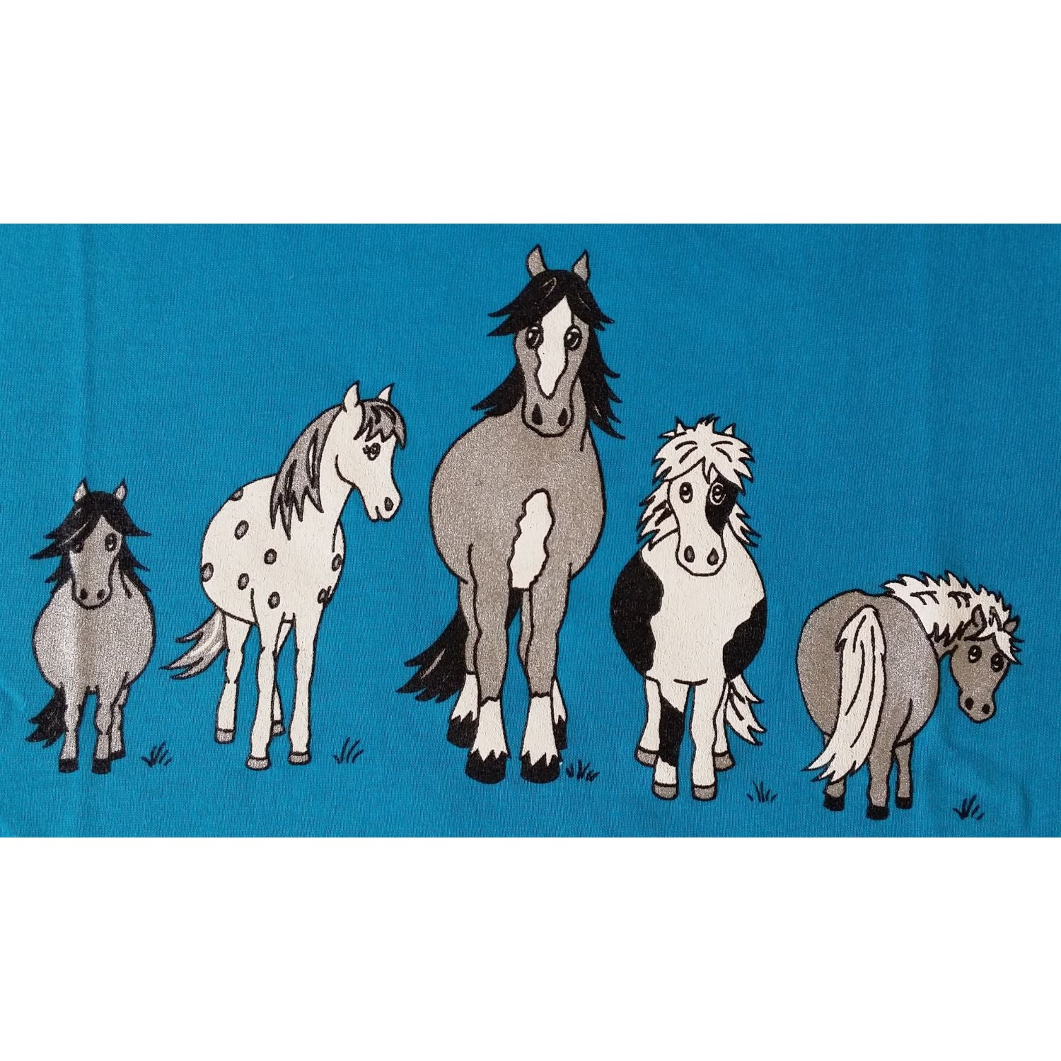 The British Country Collection Childrens T Shirt Printed The Herd Horse Design features five colorful cartoon horses and ponies standing side by side on a blue backgroundâ€”ideal for any young horse fan.