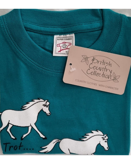 A teal Childrens Printed Horse T Shirt by British Country Collection, featuring white horse illustrations and Trot, Canter, Jump text, is neatly folded. The brand tag near the collar reads British Country Collection.