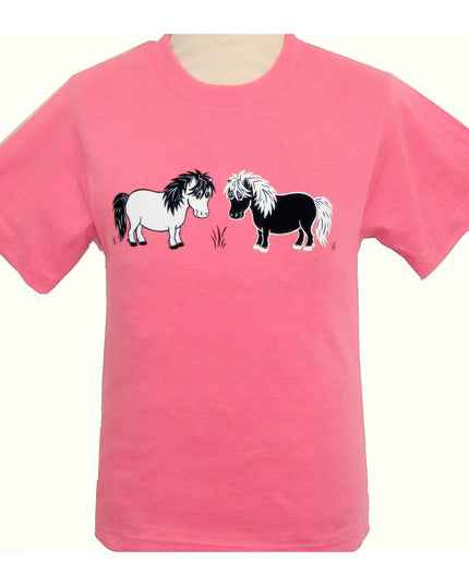 The British Country Collection Pony T Shirt Printed Pink features two cartoon Shetland ponies, one white and one black, facing each other with grass between them. Perfect for children who love ponies!.