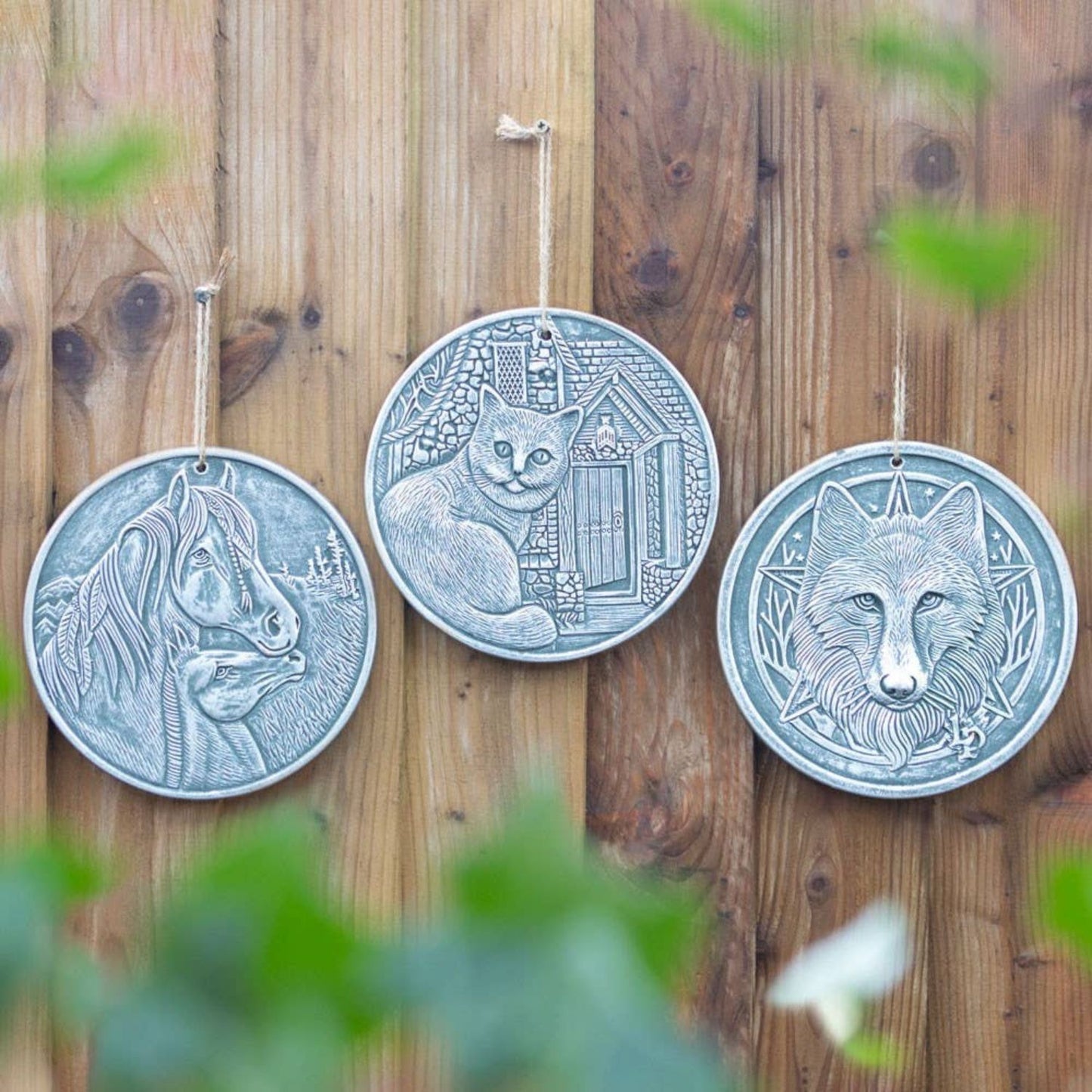 a group of 3 silver plaques featuring horses, cats and wolves on a garden fence.