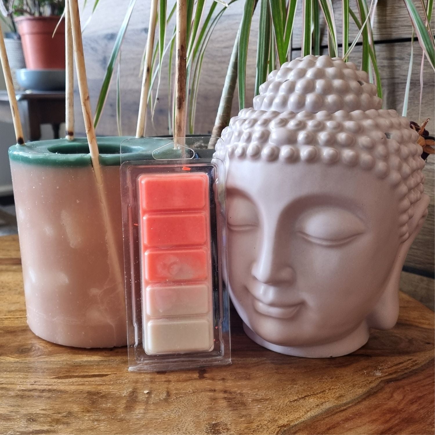  an orange and white wax melt bar in a clamshell next to a buddha's head wax warmer
