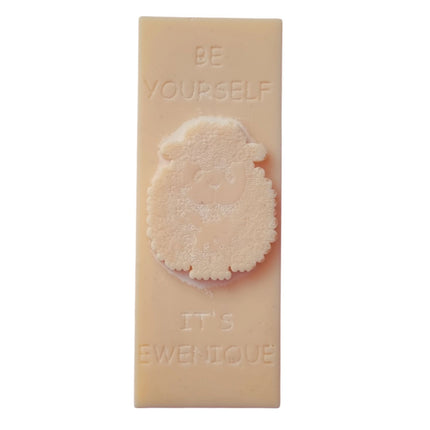 A light brown wax melt bar with a raised sheep design with the writing be yourself above and it's ewenique below.