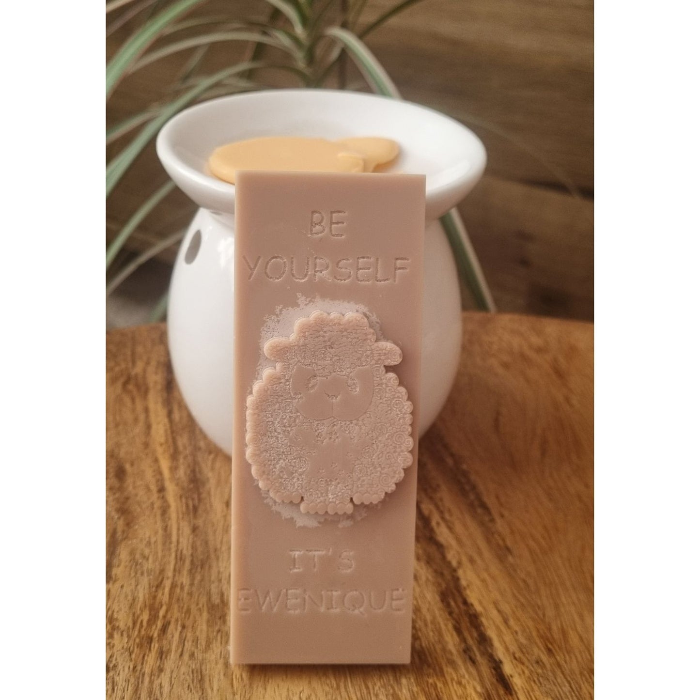 A brown coloured wax melt bar with a raised sheep design with the writing be yourself above and it's ewenique below next to a wax warmer