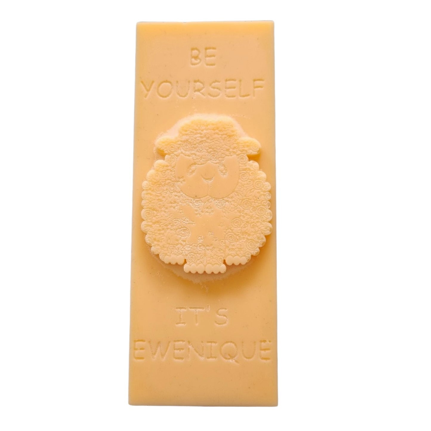 An orange coloured rectangle of wax with a raised sheep design with the writing be yourself above and it's ewenique below.