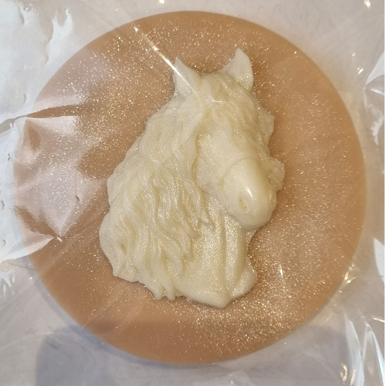 A brown coloured disc shaped wax melt with a white wax horses head with a flowing mane and forelock.