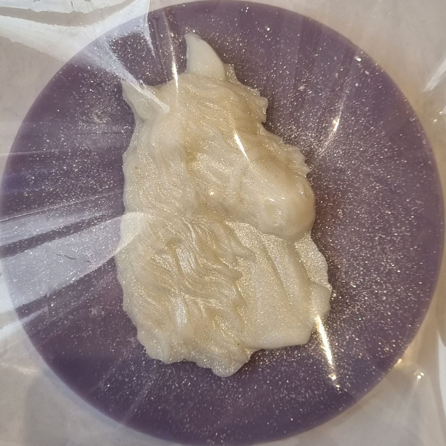 A violet coloured disc shaped wax melt with a white wax horses head with a flowing mane and forelock.