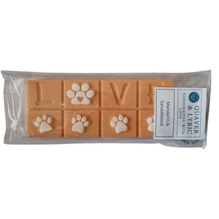 A packet with quaver and lyric branding containing an orange Scented Wax Melt bar with love and white paw prints 
