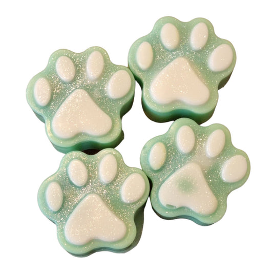 A group of four pale green wax paws with white paw pad accents with a coating of glitter.