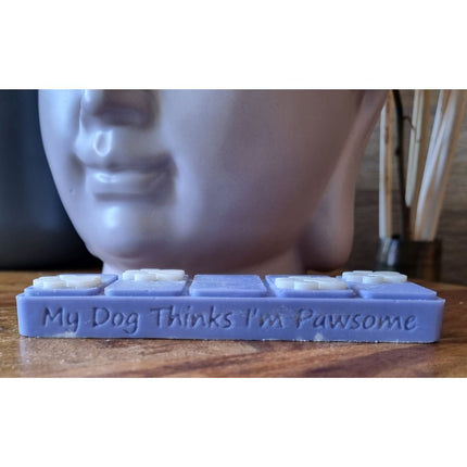 the side view which reads my dog thinks im pawsome of a blue wax melt bar with white paw prints on a wooden table next to a buddha head wax warmer