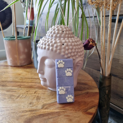 the top view of a blue wax melt bar with white paw prints on a wooden table resting against a buddha head wax warmer