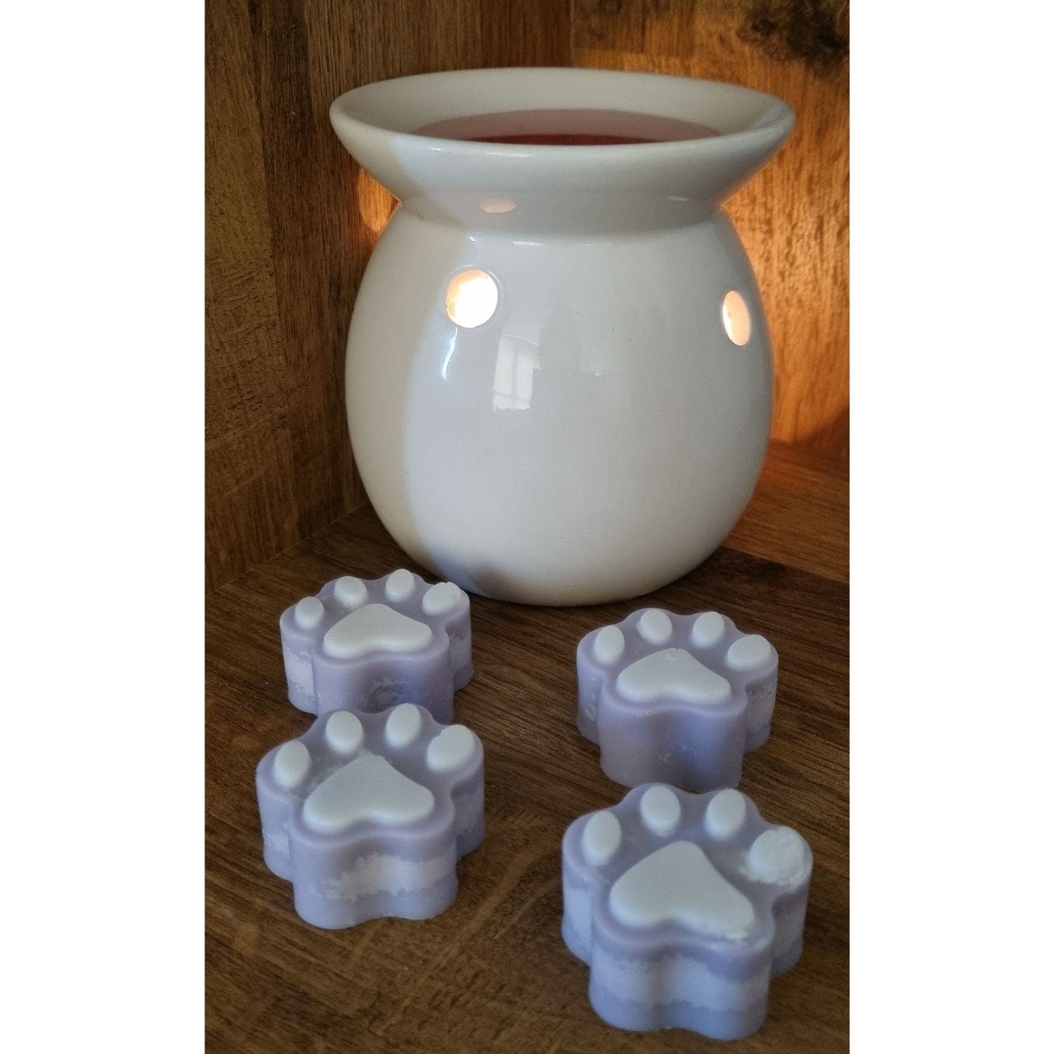 a group of four violet paw shaped wax melts with white paw pads next to a wax warmer