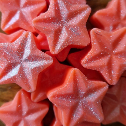 Close-up of Quaver&Lyric Soy Wax Melt Stars, a pack of 15 red, glittery soy wax melts, clustered on a wooden surface—perfect for filling your space with fragrance.