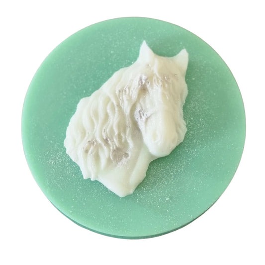 A green coloured disc shaped wax melt with a white wax horses head with a flowing mane and forelock.