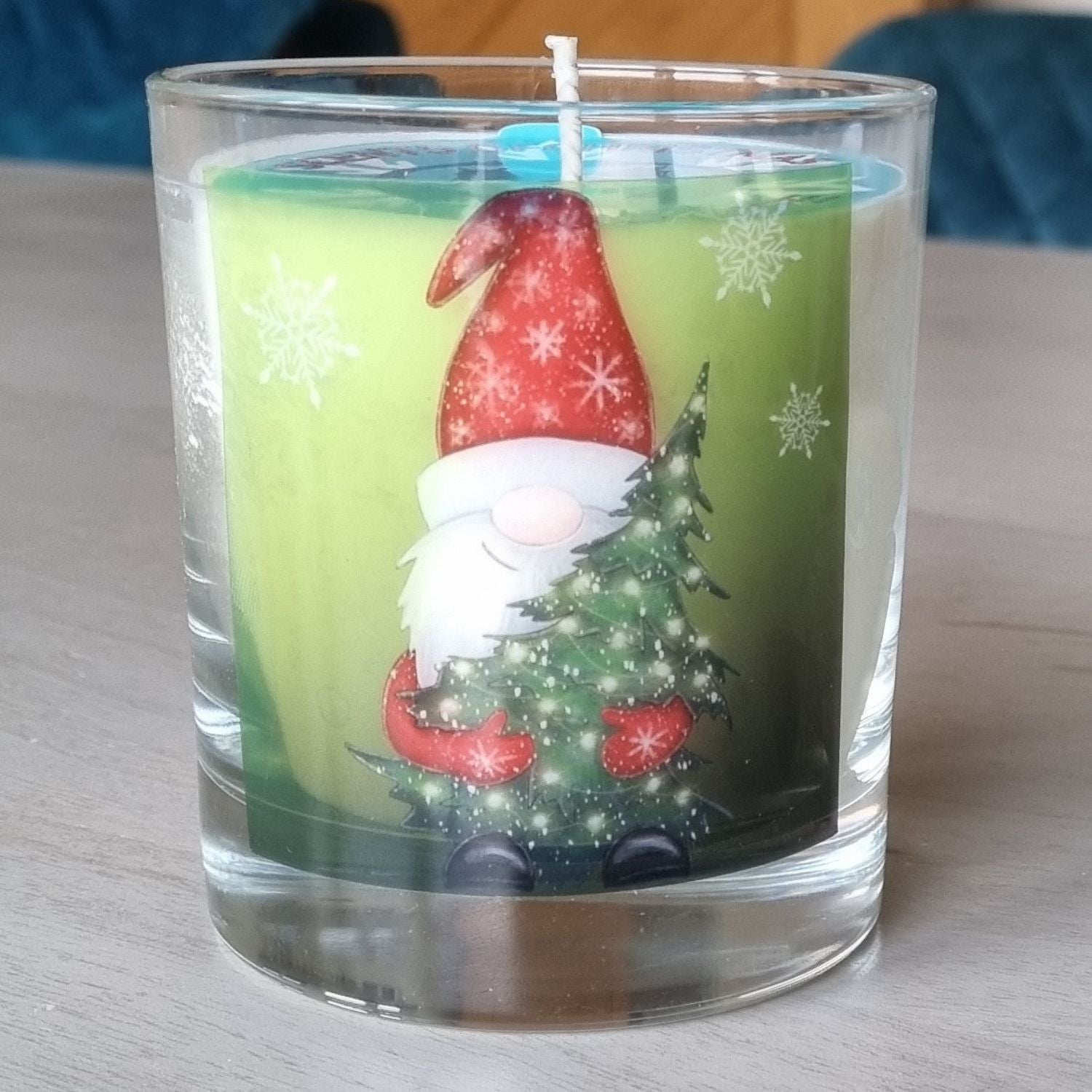 Father Christmas candle with father christmas holding a christmas tree design on the front of a scented candle in glass container. The candle is on a table.