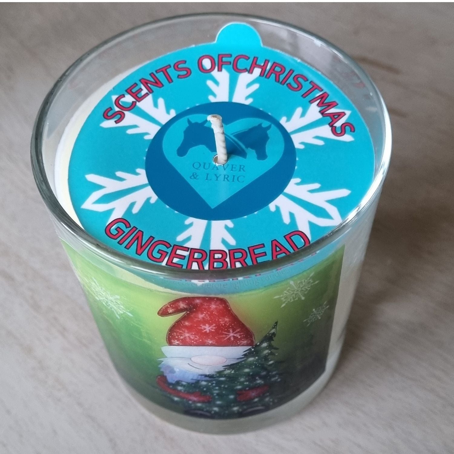 The view from above showing the dust cover of a Father Christmas candle with father christmas holding a christmas tree design on the front of a scented candle in glass container