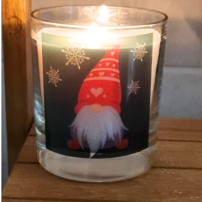 a burning scented candle in a glass container with a Christmas gonk design