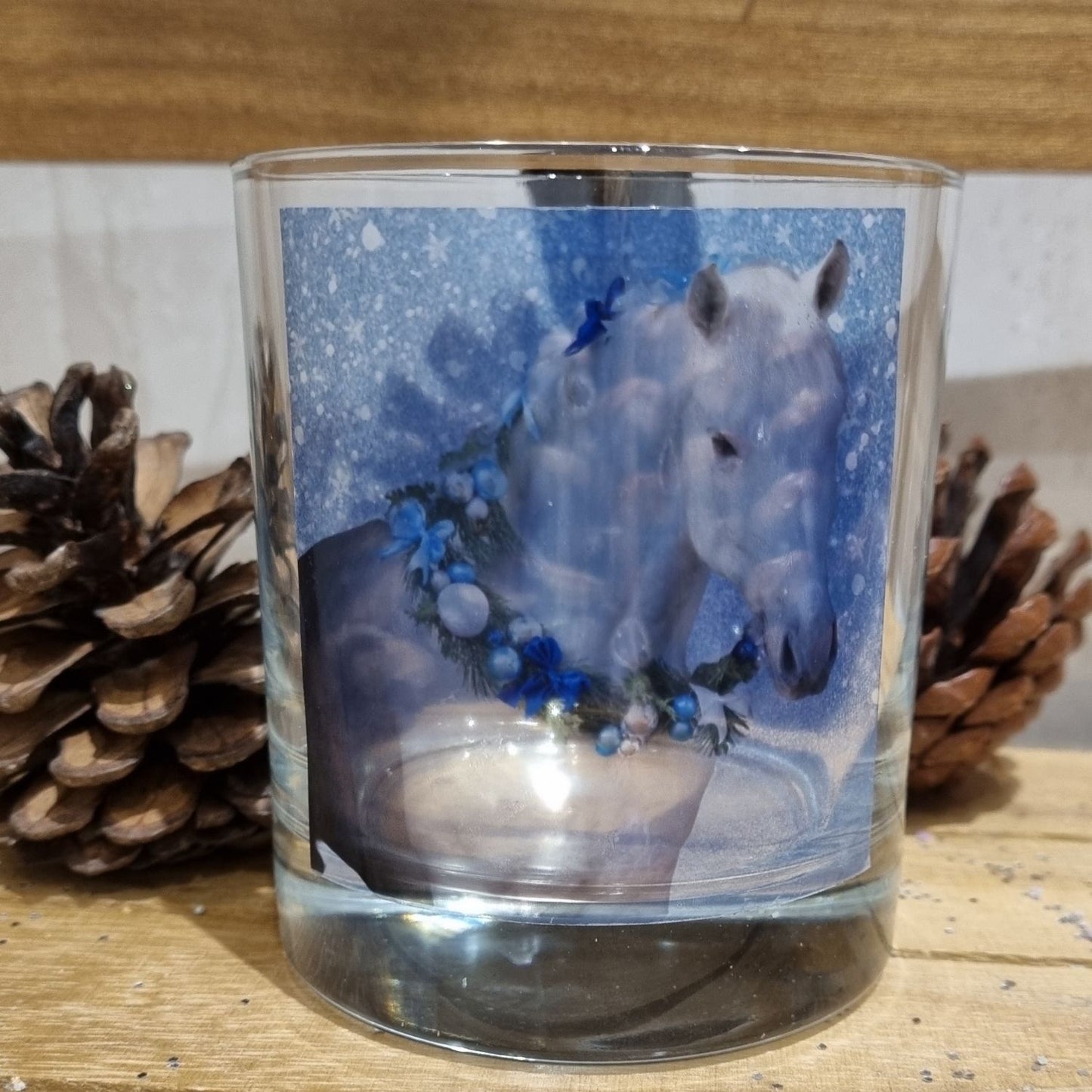 a close up shot of an empty scented candle glass container decorated with a grey horse wearing a festive garland on his neck