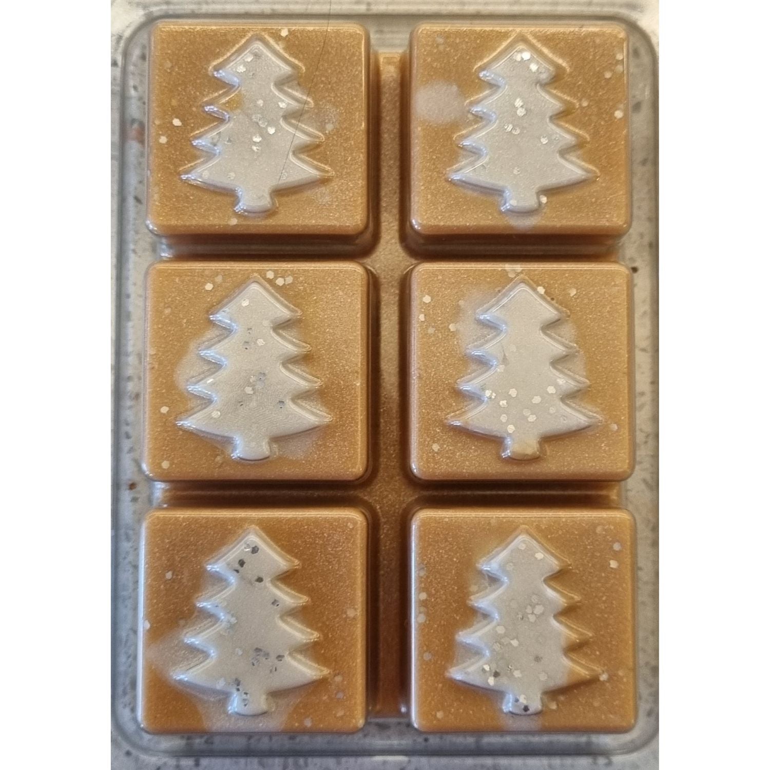 Christmas fragrance wax melts in a Christmas tree design clamshell. With white scented wax christmas trees on golden brown scented cubes.